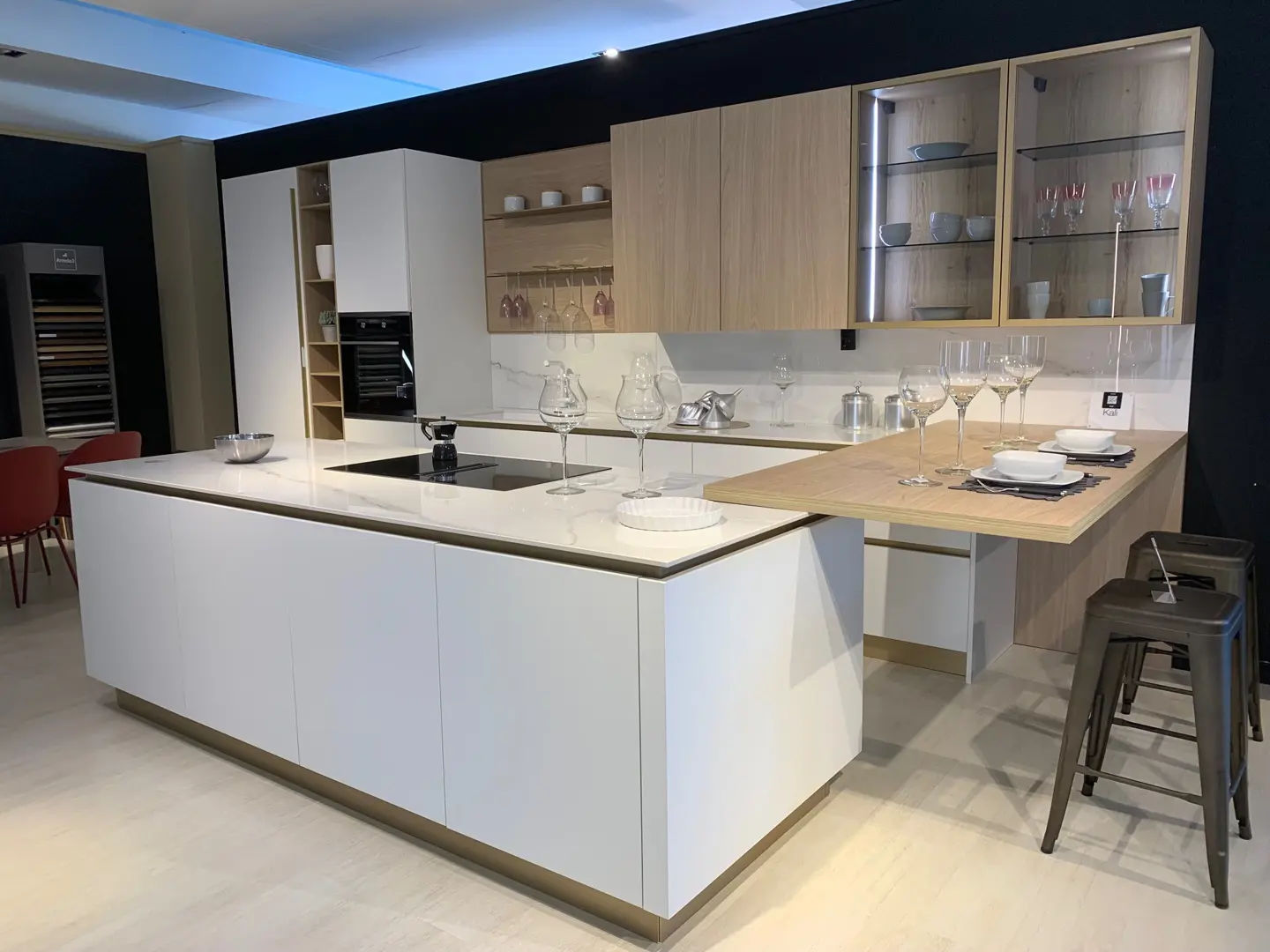 Cucina Kali di Arredo3, composizione top di gamma con isola centrale bianca e boiserie in legno naturale, esposta nello showroom Arredamenti Soldi a Follonica